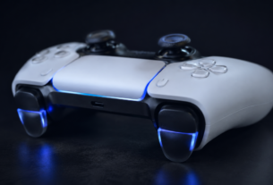 Controle profissional ps5 sem fio para console com gatilhos adaptativos iluminados em azul sobre superfície escura com iluminação dramática lateral.