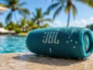 Aparelho de som portátil caixa de musica jbl azul com gotas de água posicionado na borda de uma piscina ensolarada