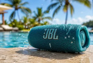 Aparelho de som portátil caixa de musica jbl azul com gotas de água posicionado na borda de uma piscina ensolarada
