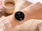 Dispositivo do tipo relógio feminino smartwatch rosa delicado no pulso de uma mulher sobre mesa de madeira decorada