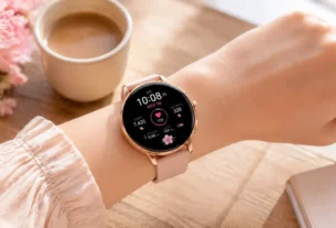 Dispositivo do tipo relógio feminino smartwatch rosa delicado no pulso de uma mulher sobre mesa de madeira decorada