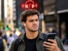 Homem na rua olhando o celular frustrado com fone bluetooth cortando audio em ambiente urbano
